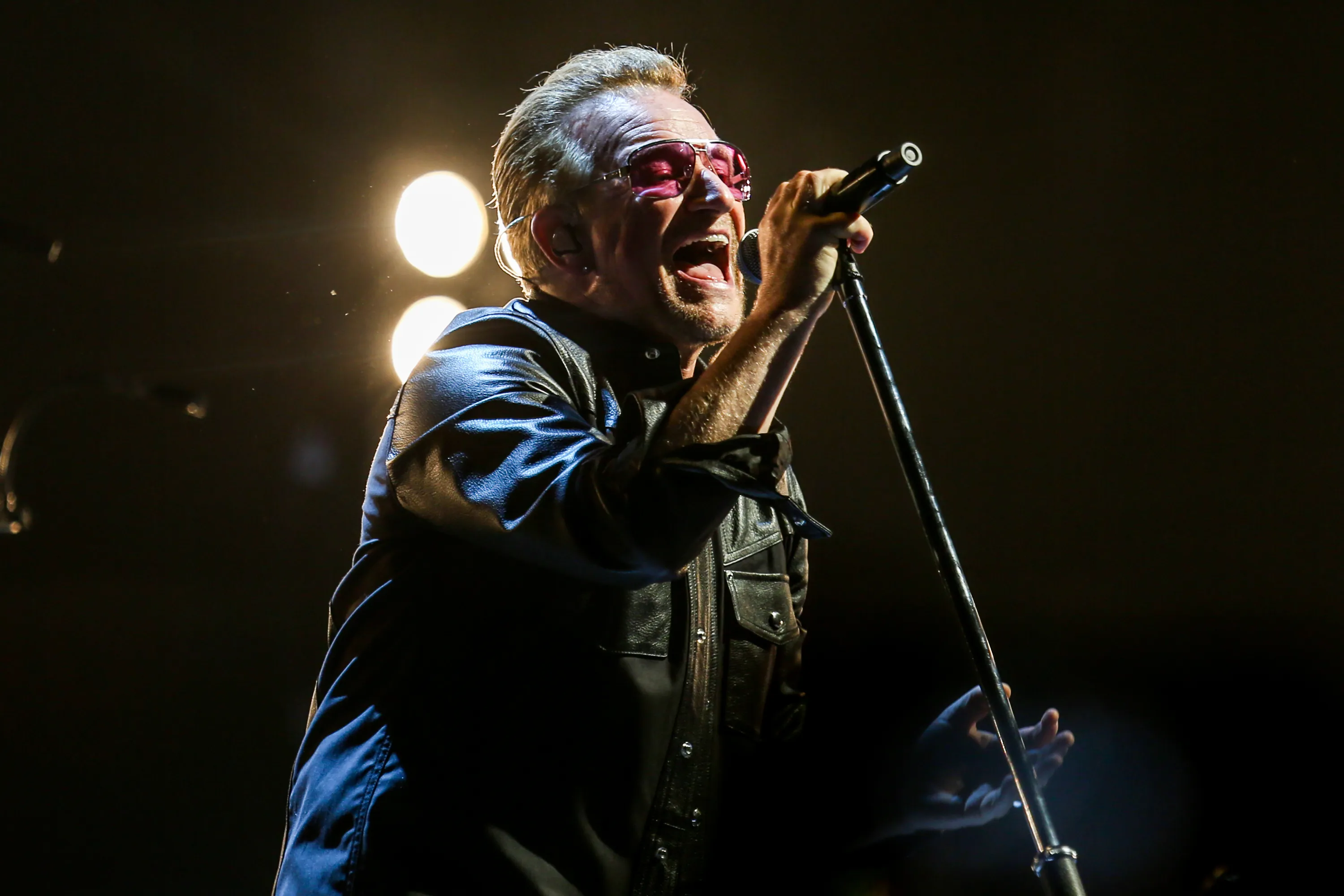 Bono of U2 performing on stage with a microphone.