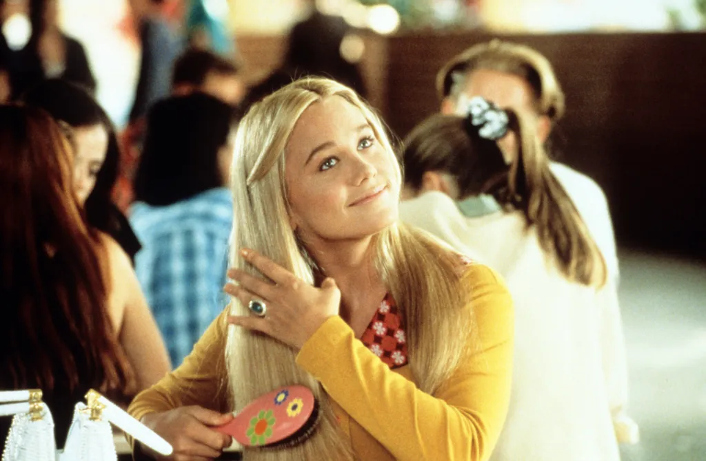 Christine Taylor brushing her long blonde hair with a pink brush.