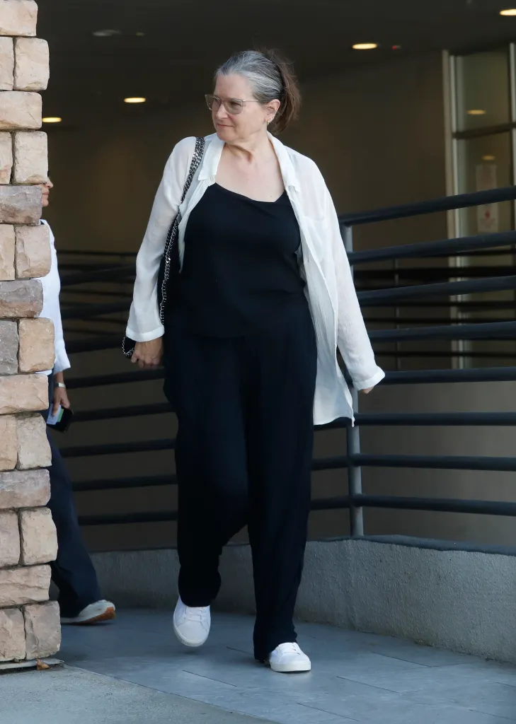 Bridget Fonda wearing a white blouse, black top, black trousers, and white trainers while stepping out in Los Angeles.