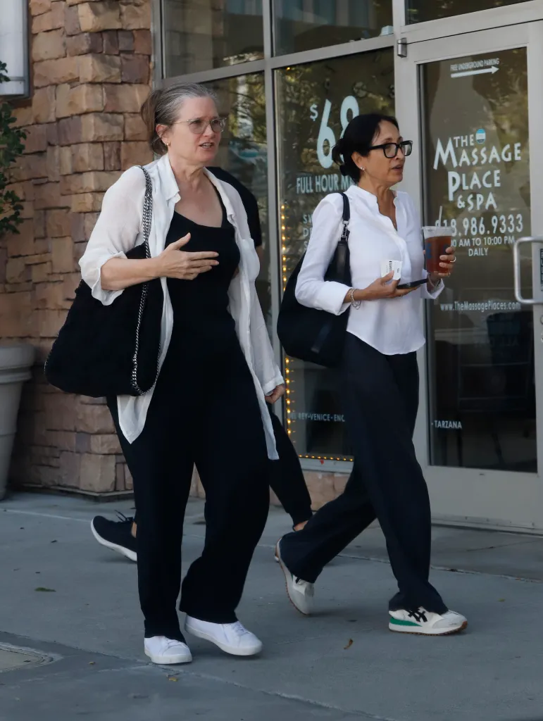 Bridget Fonda, in a white blouse and black outfit, walks next to another woman.