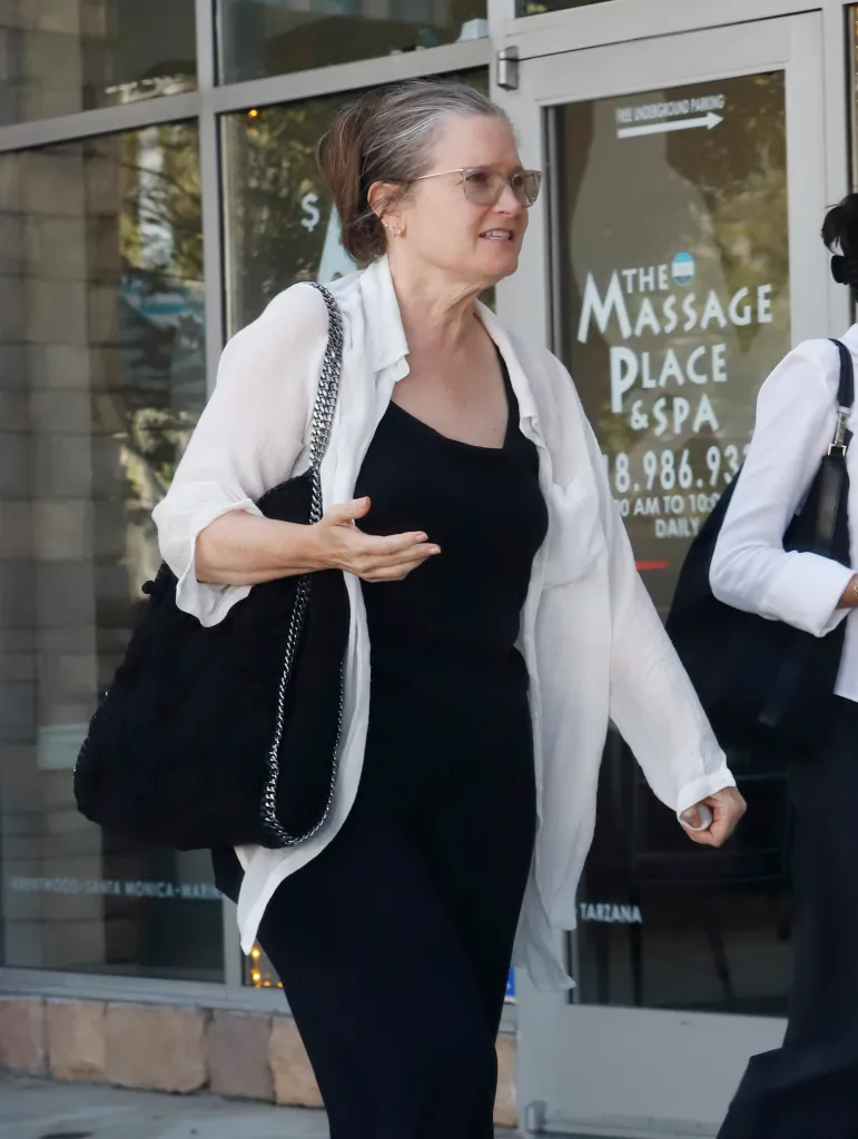 Bridget Fonda, in a white blouse and black outfit, walks past 