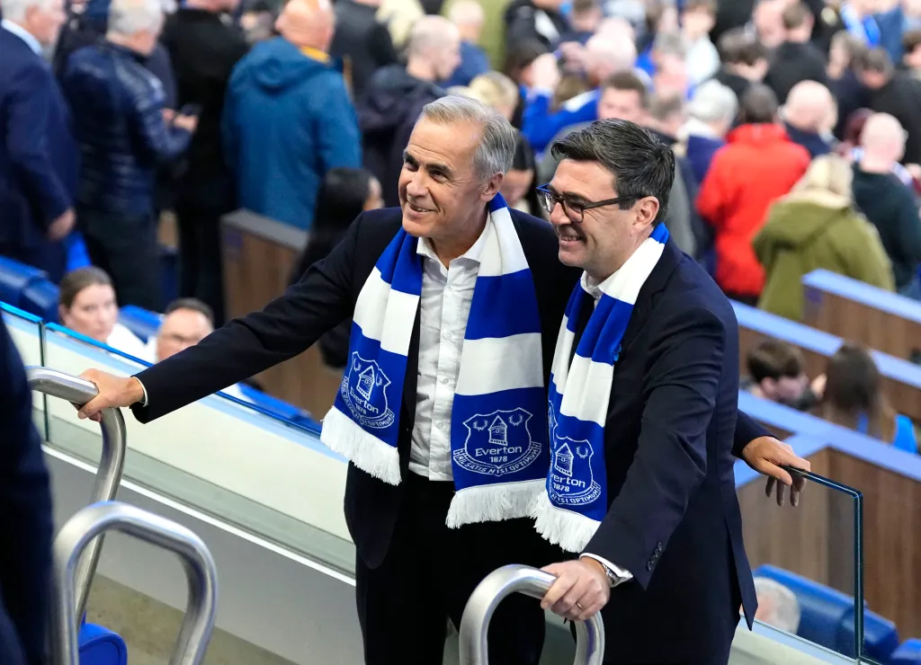 Britain's Prime Minister Andy Burnham and Canada's Prime Minister Mark Carney wearing Everton scarves at a soccer match.
