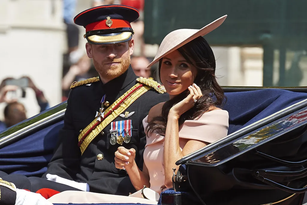 Prince Harry in military uniform and Meghan, Duchess of Sussex, in a pale pink dress and hat, riding in a horse-drawn carriage.