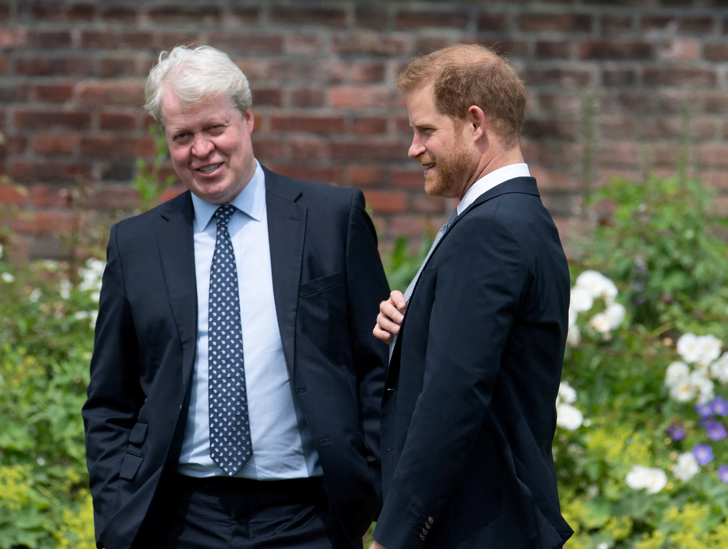 Prince Harry and his uncle Charles Spencer in suits, conversing outdoors.