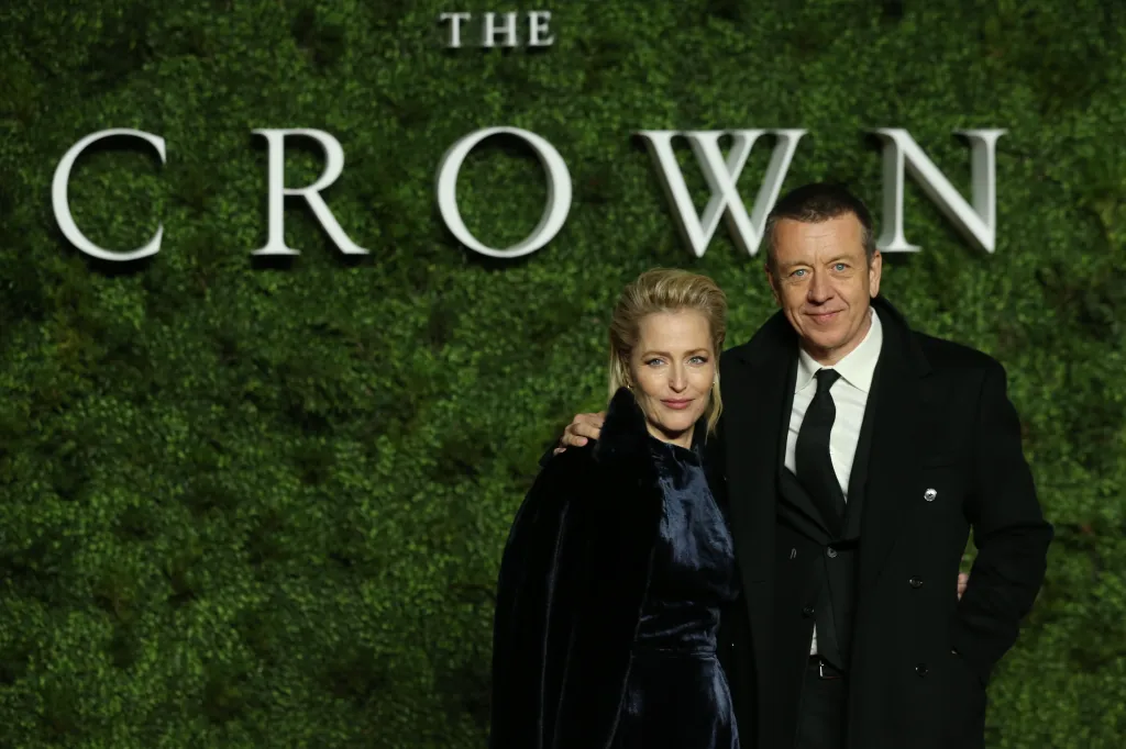 Gillian Anderson and Peter Morgan pose on a red carpet in front of a green moss wall with 