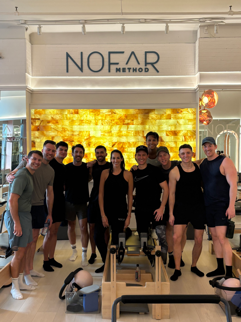 Group photo of nine men and one woman in athletic wear at a Bro-Lates pilates class at The Nofar Method.