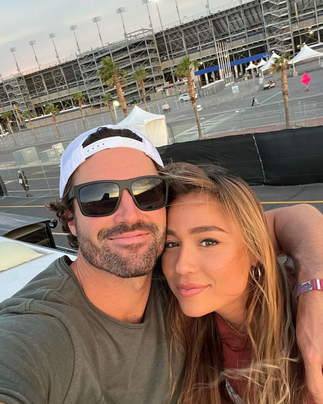 Brody Jenner and Tia Blanco pose for a selfie with a stadium and palm trees in the background.
