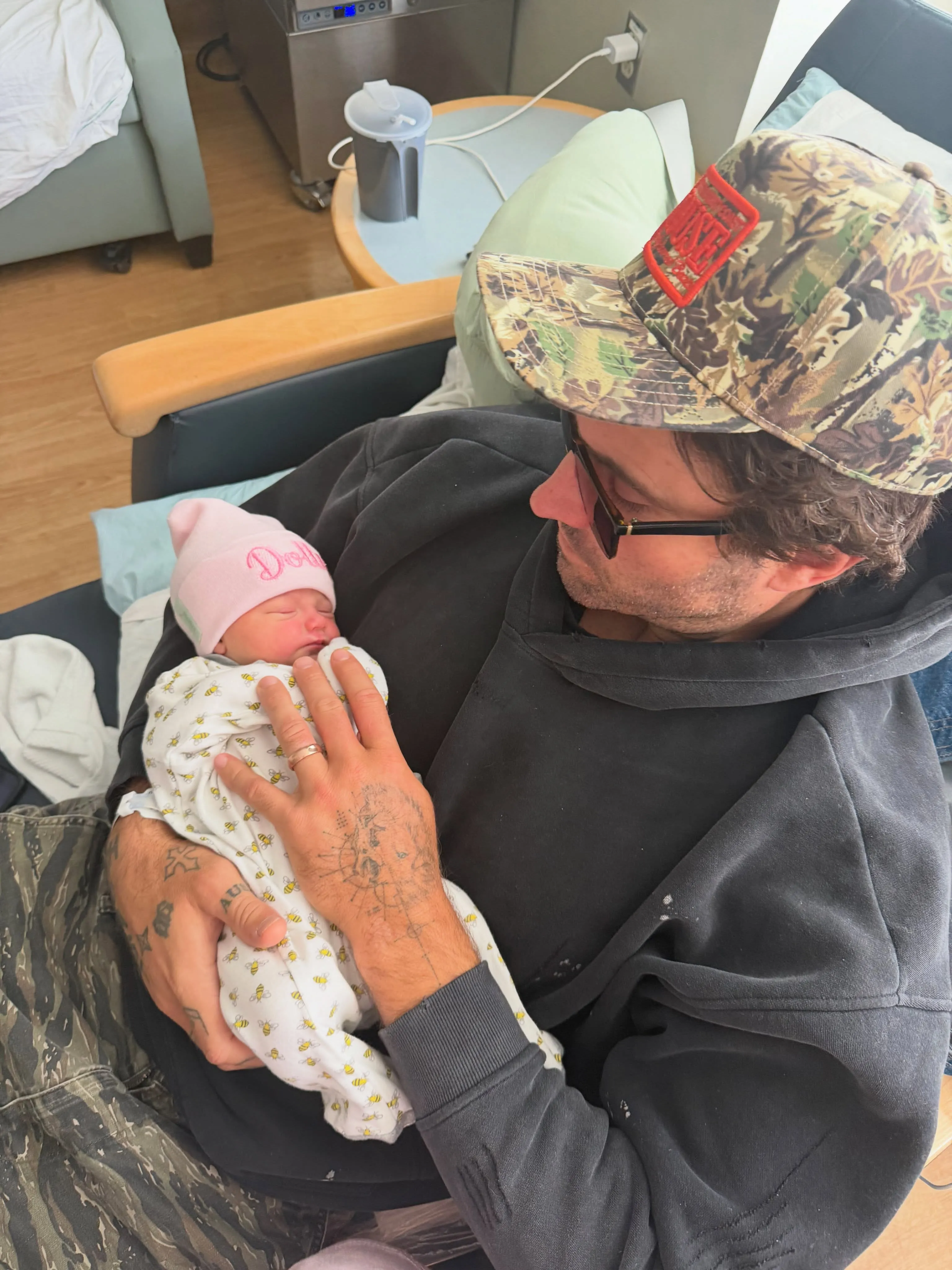 Brody Jenner holds his new baby, Dolly Jane, who wears a pink hat with 