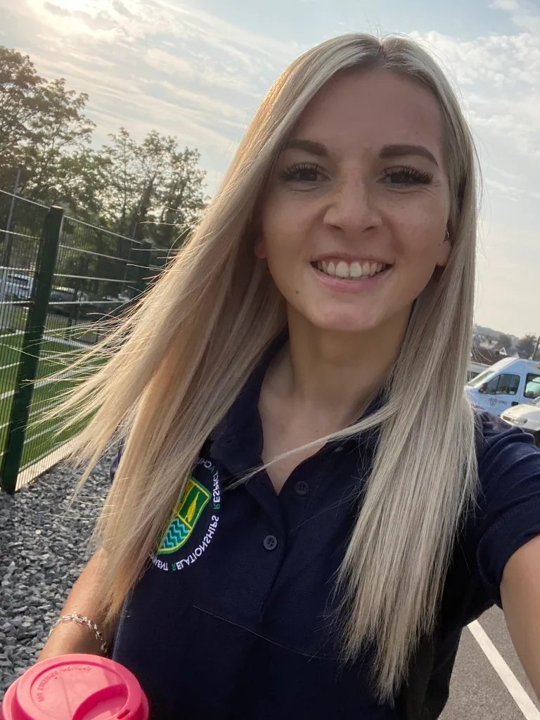 Bronwen James, a PE teacher with blonde hair, smiling for a selfie outdoors.