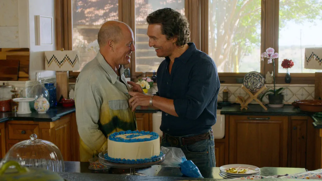 Woody Harrelson and Matthew McConaughey in a kitchen, celebrating with a birthday cake.