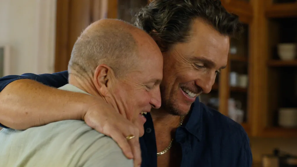 Two men, one bald and one with dark hair, embrace and laugh.