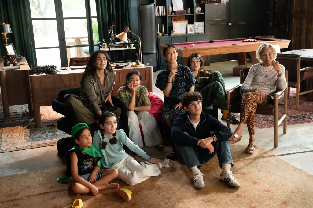 A group of multi-generational people of various ethnicities watching something off-camera in a living room with a pool table.