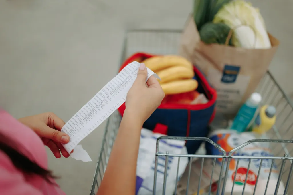 Hands hold a long paper receipt with a full shopping cart in the background.