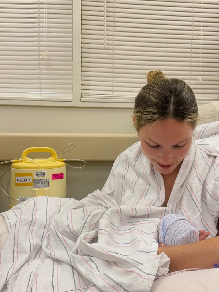 Natasha Bure, Candace Cameron Bure's daughter, holding her newborn in a hospital bed with a NICU machine nearby.