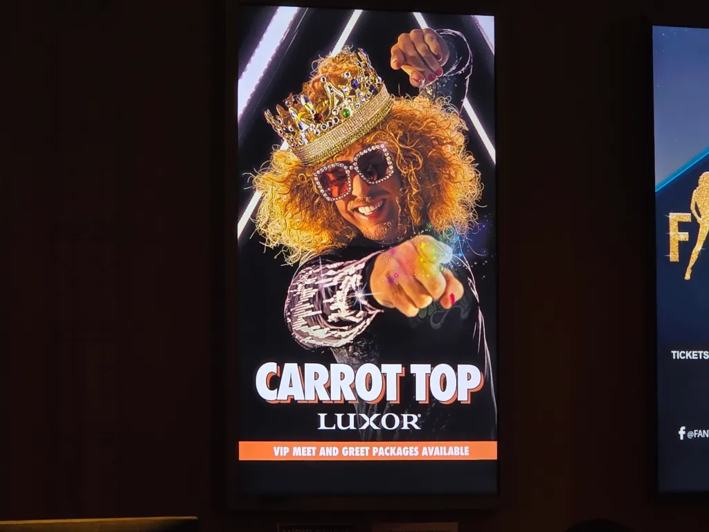 Promotional poster for Carrot Top's show at the Luxor, featuring the comedian in a crown and sunglasses, pointing forward.