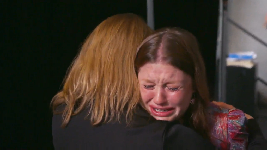 Catie crying while being consoled by someone with long blonde hair.
