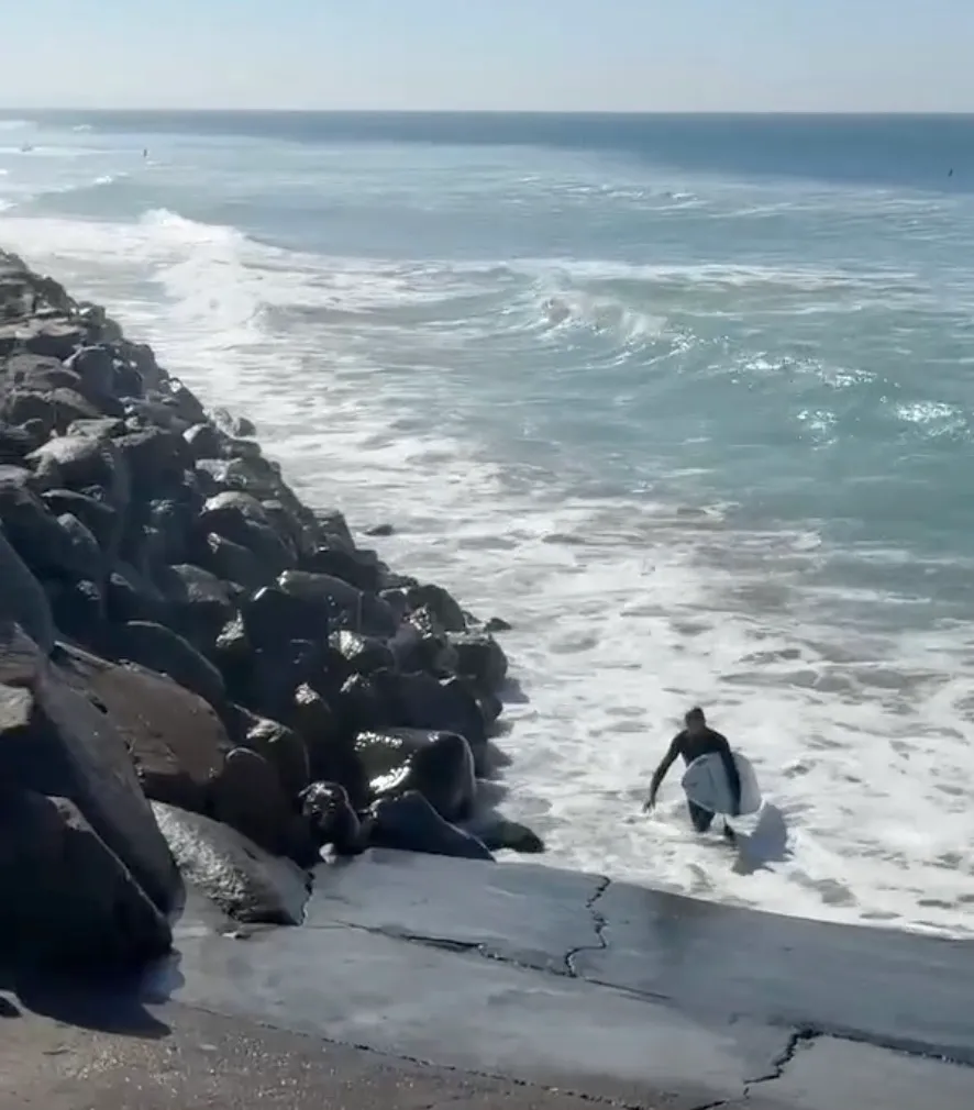 Celebrity publicist Benita Karo exiting the ocean with a surfboard after rescuing a surfer.