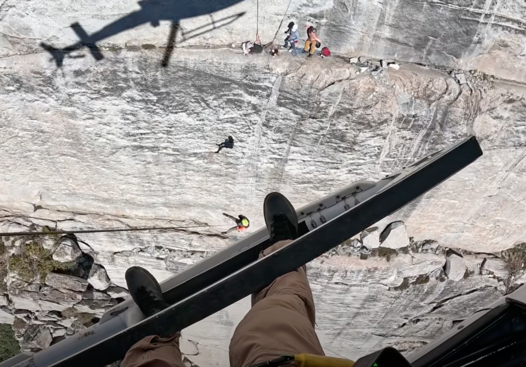 A helicopter performing a hoist extraction of an injured rock climber from a steep rock face.