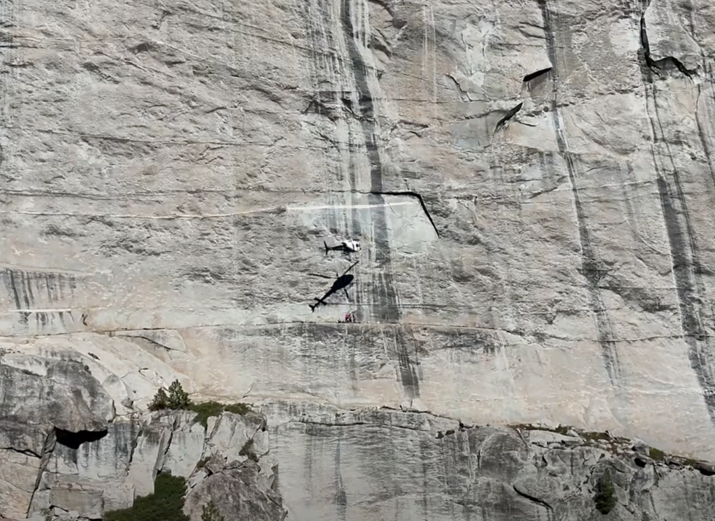 Helicopter-70 performing a hoist extraction of an injured rock climber from a cliff.