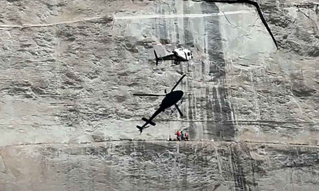 A rescue helicopter hovering over an injured rock climber on a cliff face.