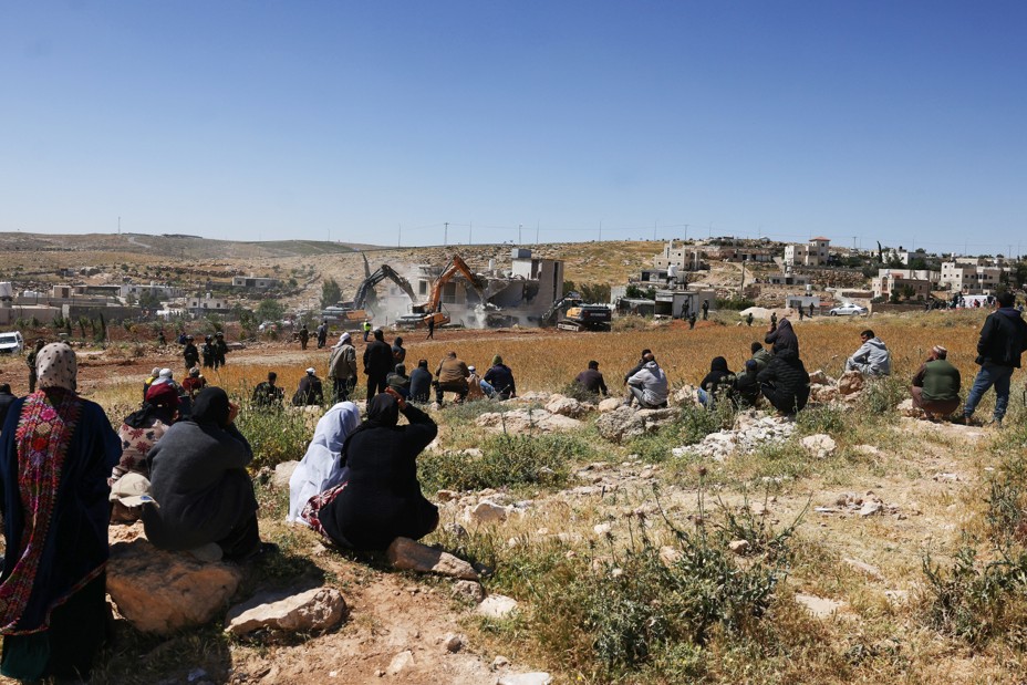 Palestinians watch as Israeli security forces stand guard while excavators demolish a Palestinian house that was built without a permit near the occupied West Bank city of Hebron