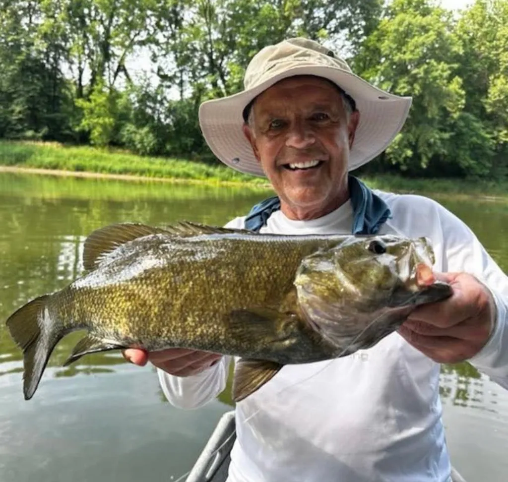 A smiling man wearing a hat and holding a large fish he has caught.