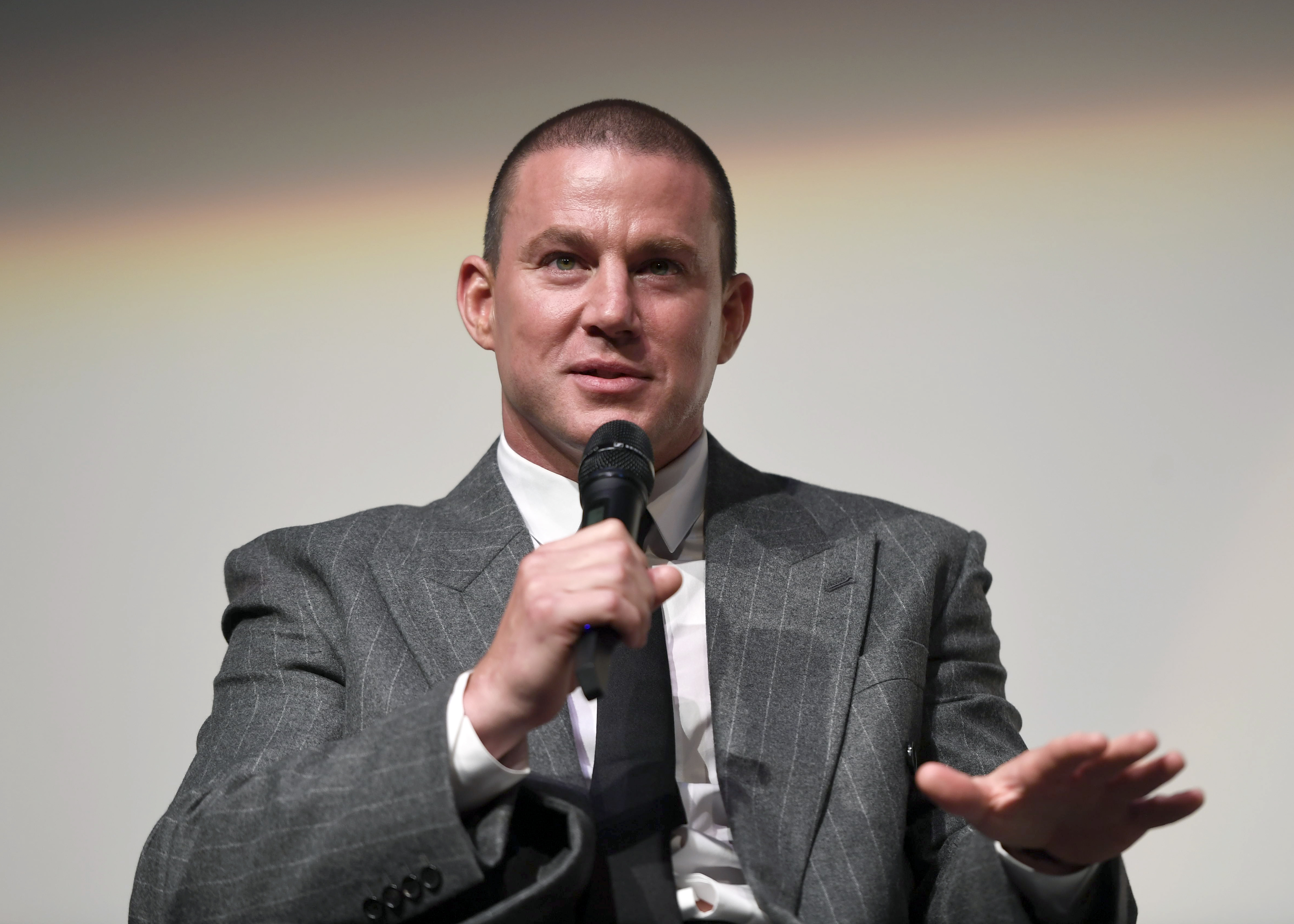 Channing Tatum speaking onstage with a microphone at the 