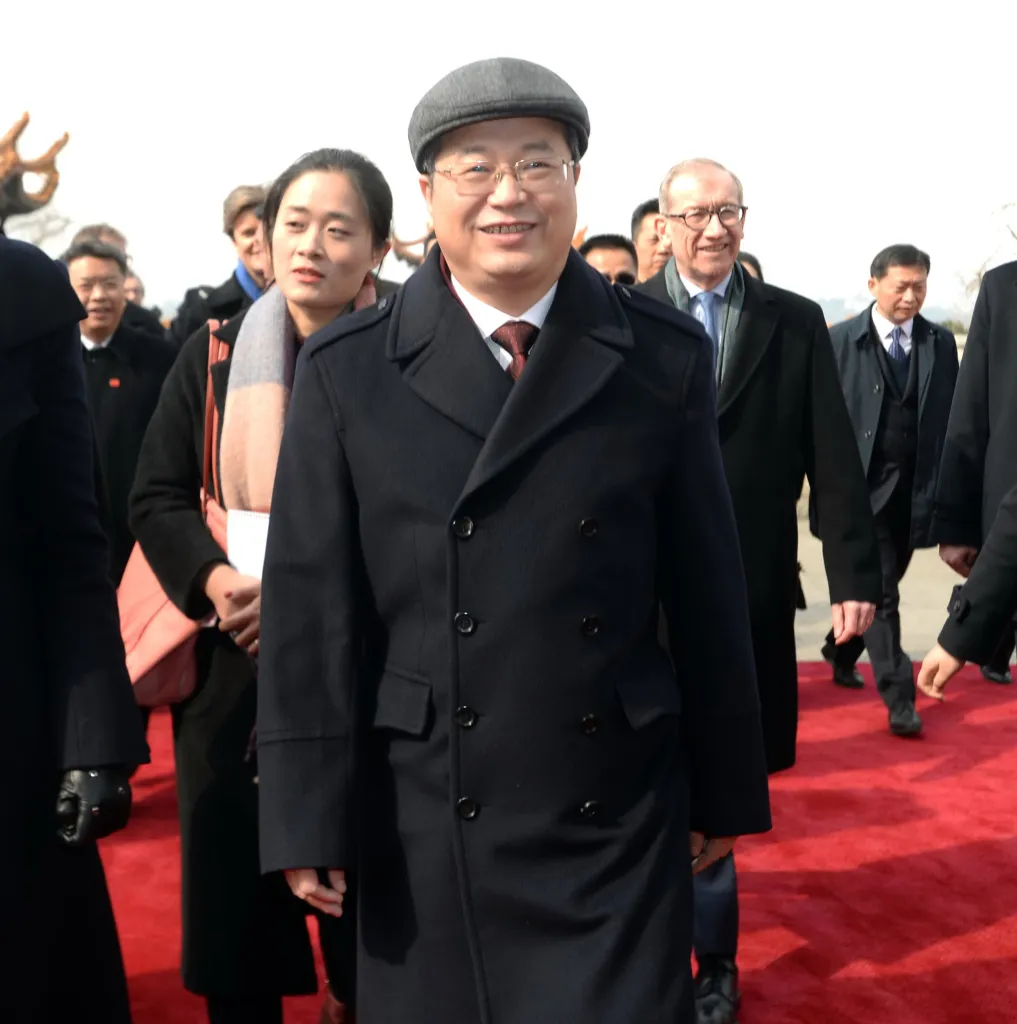 Chen Yixin, Communist Party boss of Wuhan, stands smiling on a red carpet while wearing a dark coat and cap.