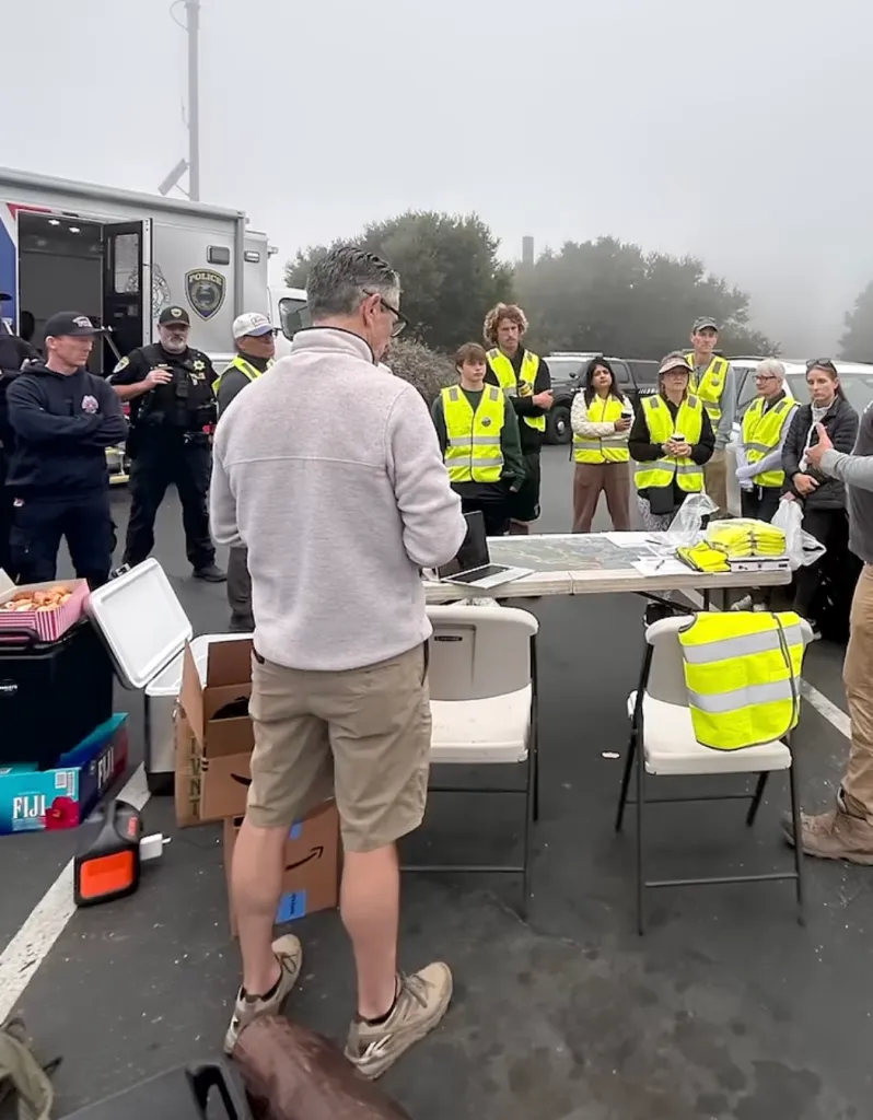Chris Hillyard speaks to investigators and volunteers, many wearing neon safety vests, about the search for his missing wife.