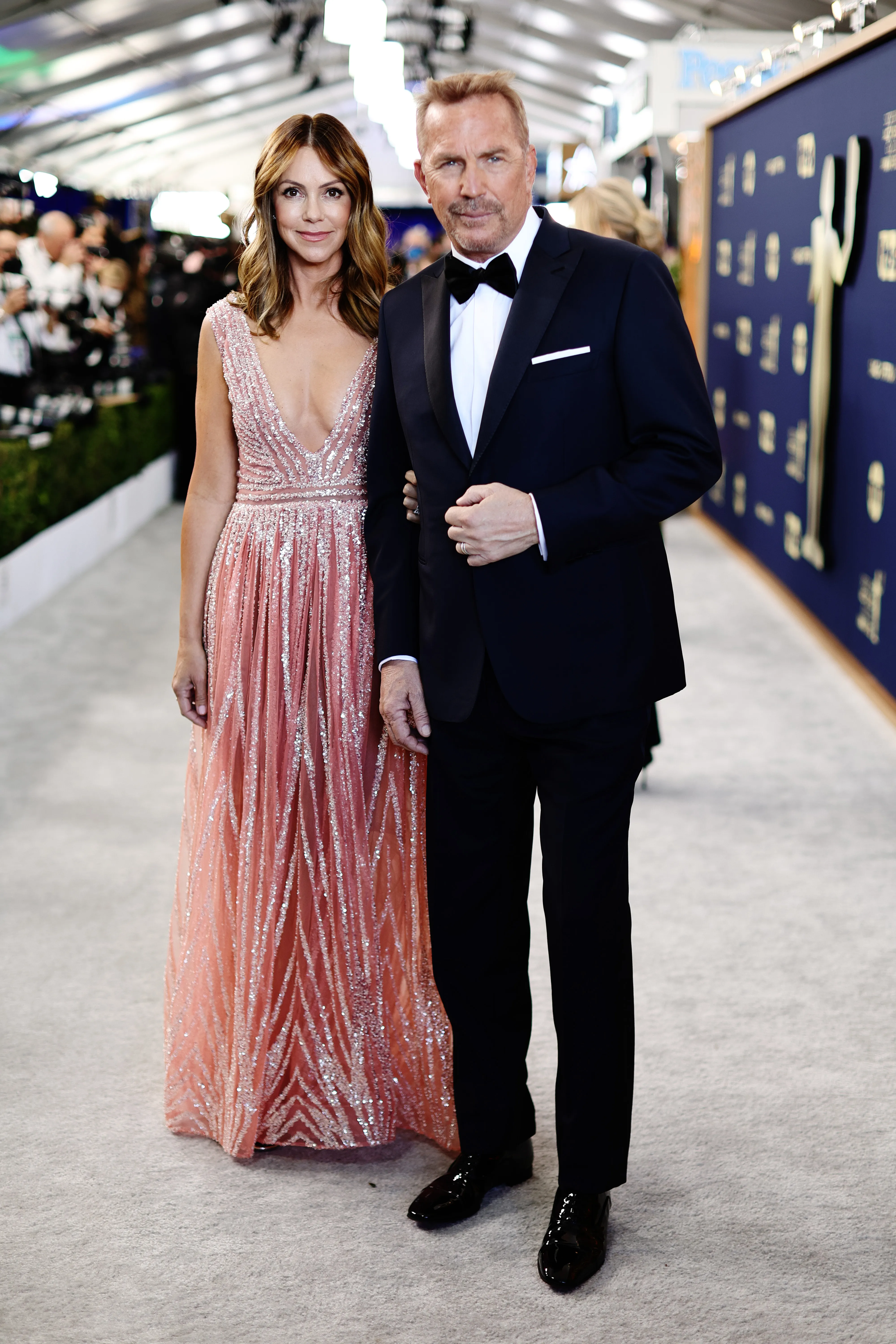 Christine Baumgartner and Kevin Costner standing together on a red carpet.