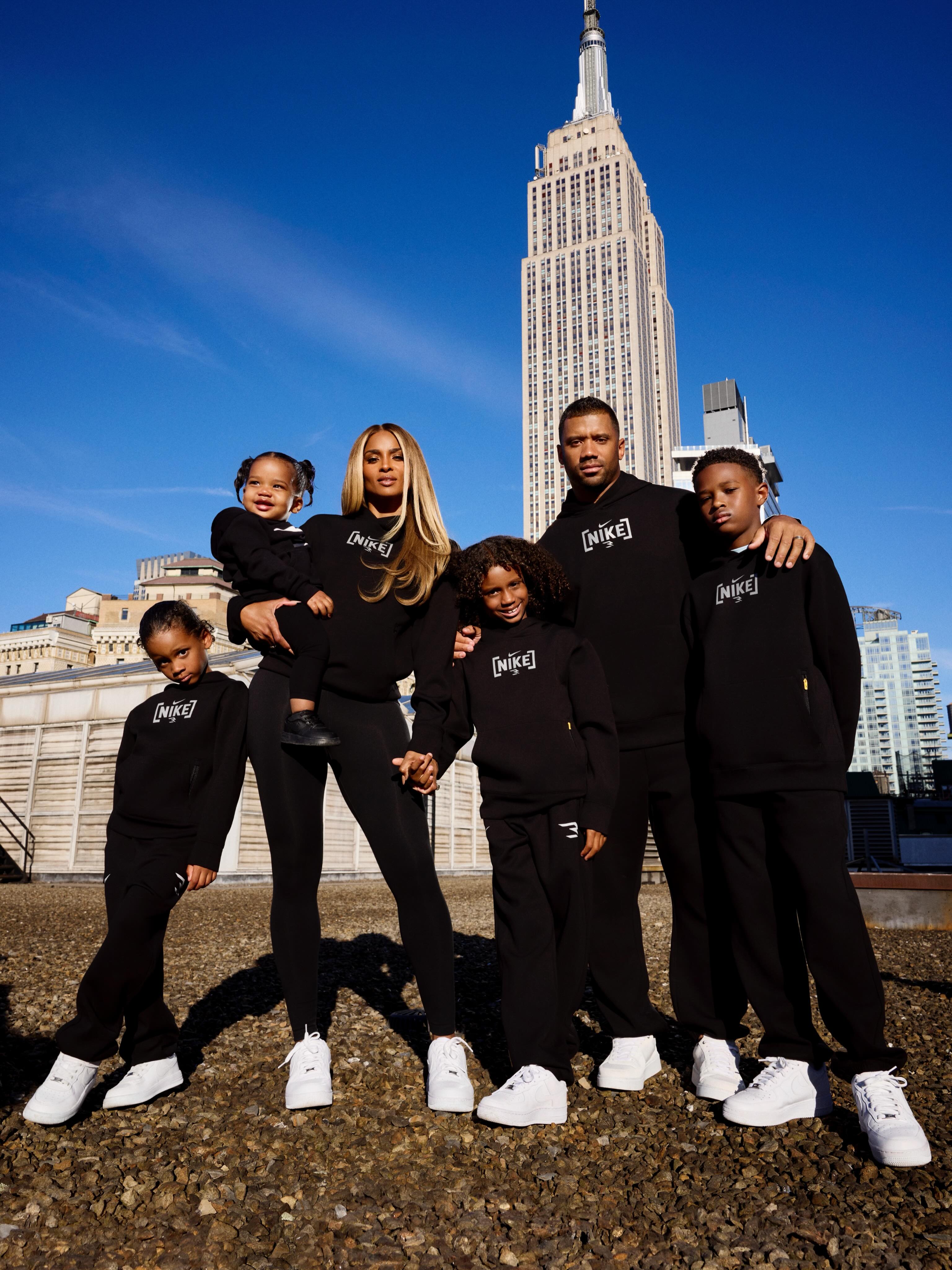 Ciara and Russell Wilson with their four children in matching black Nike outfits, standing in front of the Empire State Building.