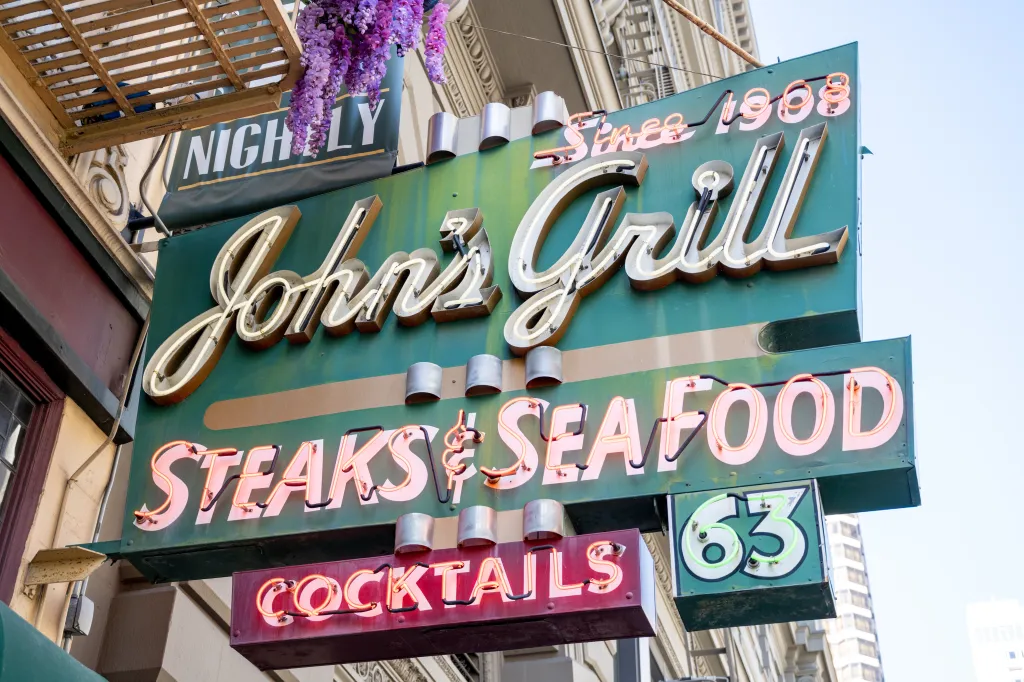A vintage neon sign for John's Grill advertises steaks, seafood, and cocktails.