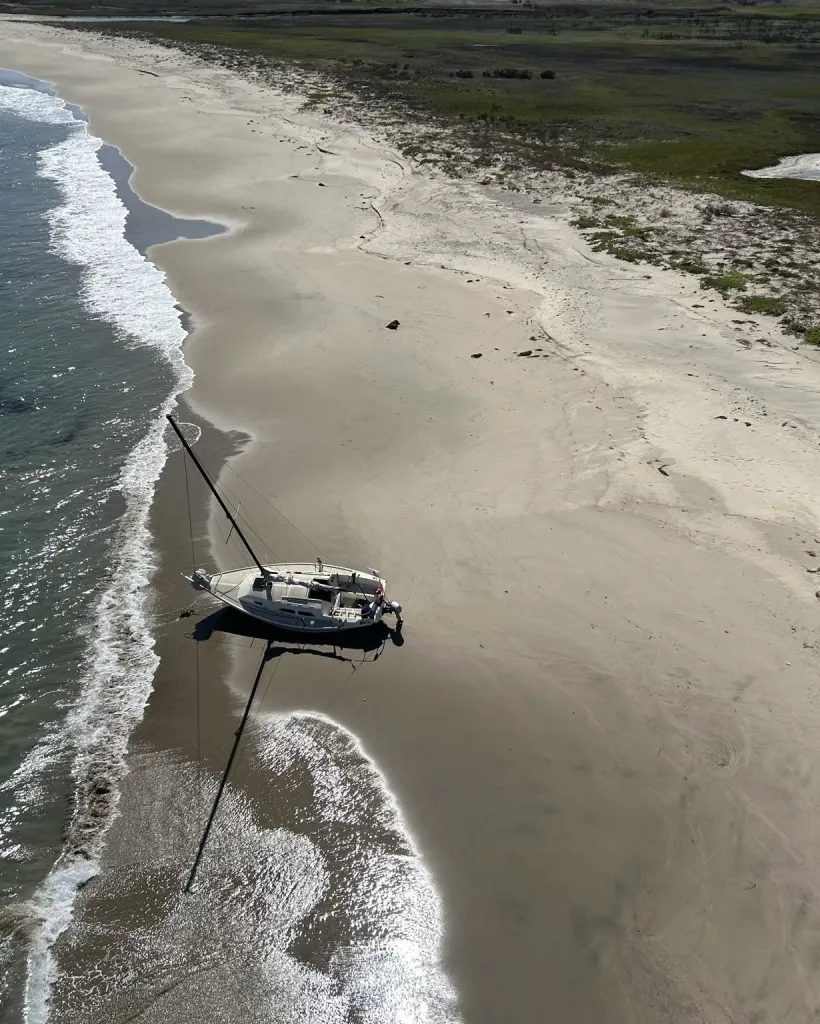 Aerial view of a sailboat grounded on a sandy beach next to the ocean.