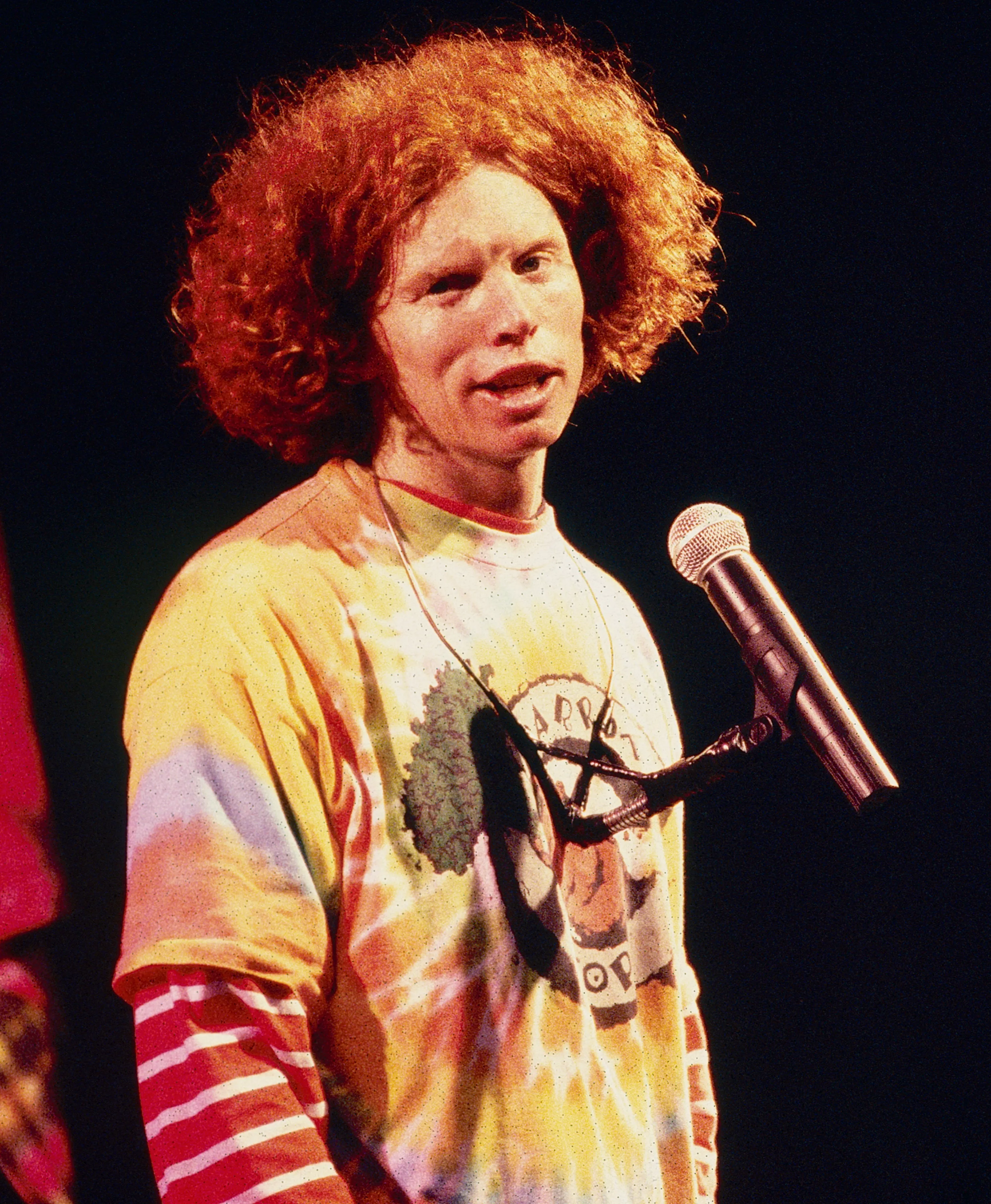 Comedian Carrot Top performing live on stage in a tie-dye shirt.