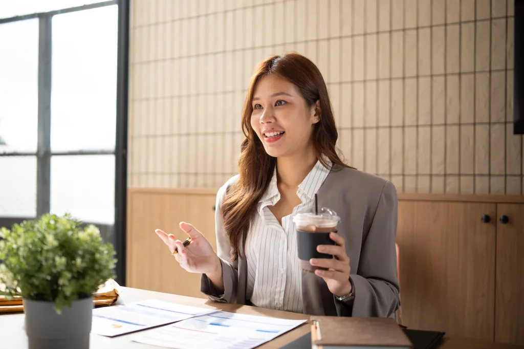 Businesswoman sitting at a desk with an iced coffee and discussing ideas.