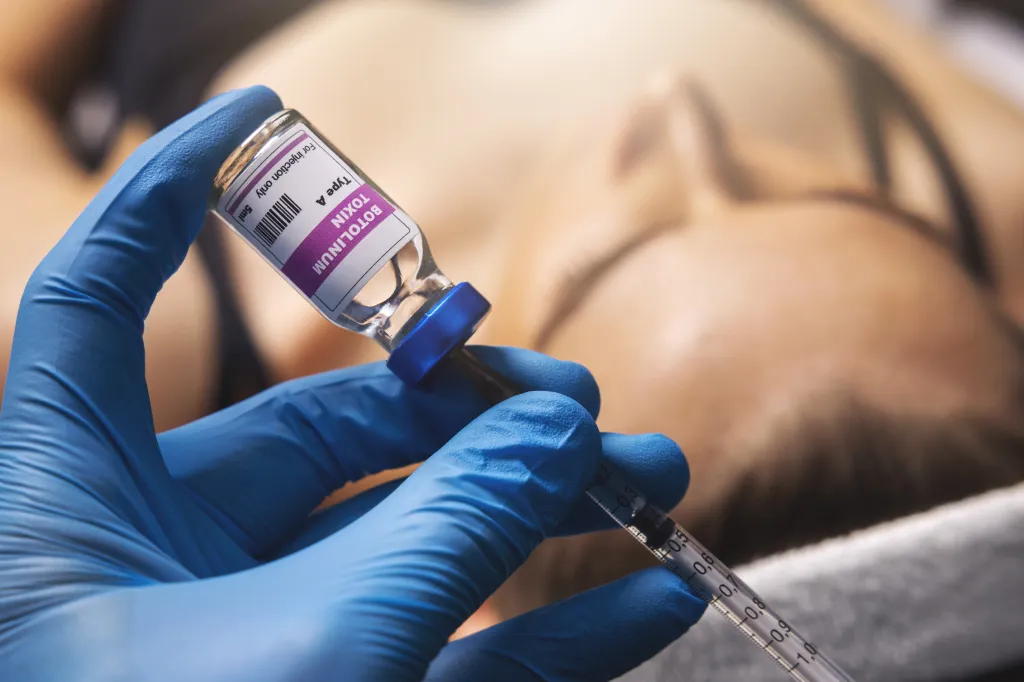 A gloved hand filling a syringe with botulinum toxin from a vial.