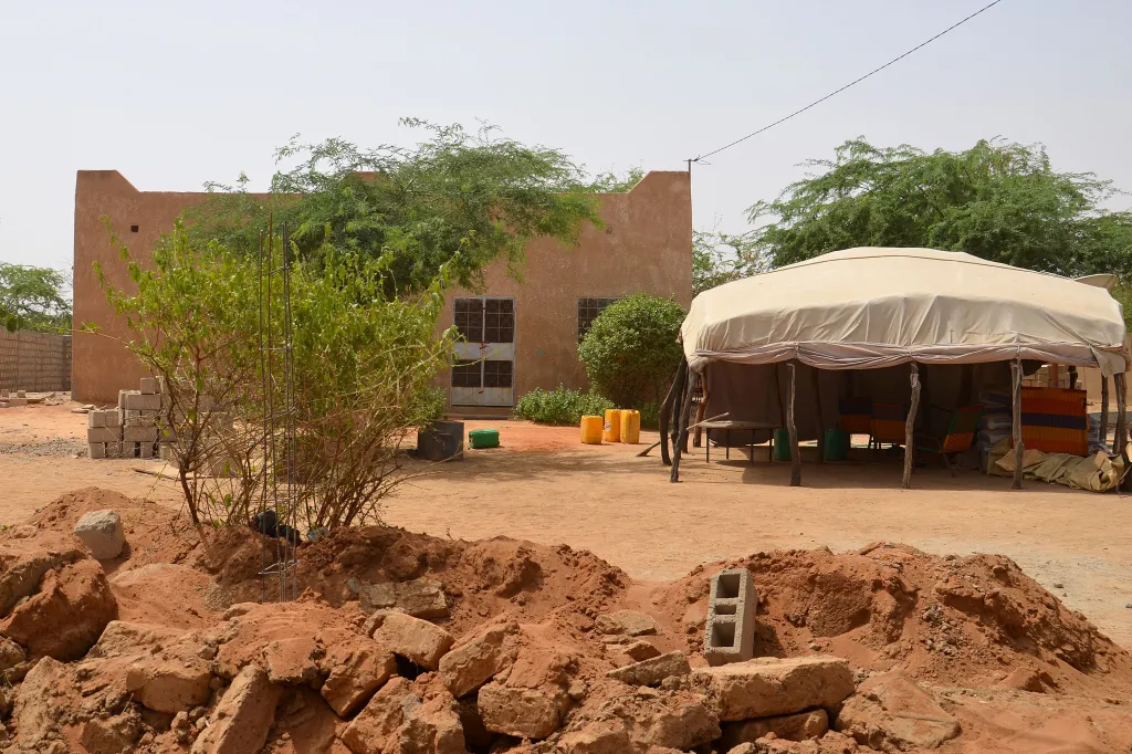 The home of U.S. aid worker Jeffery Woodke in Abalak, Niger, featuring an adobe house, green trees, a large tent, and red dirt ground.