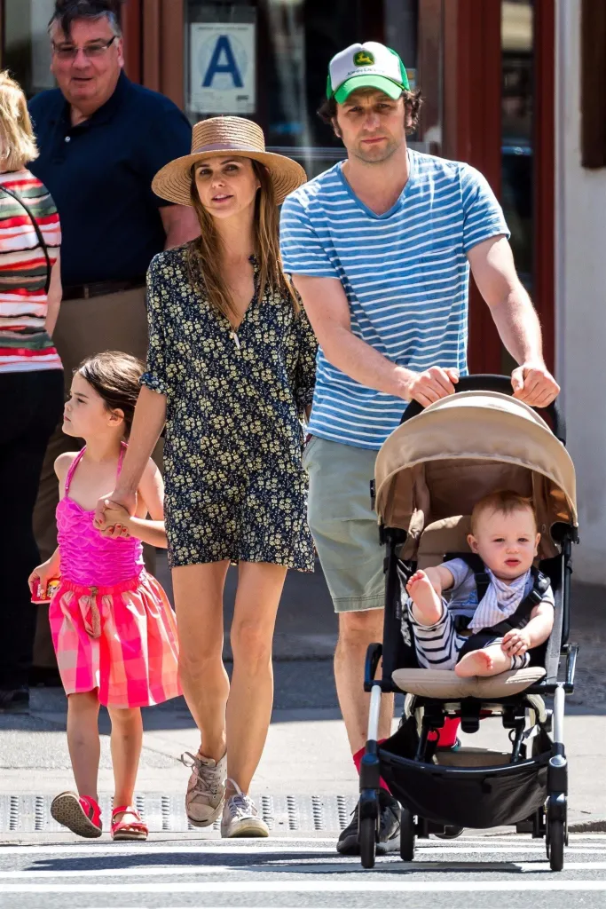 Keri Russell, in a black patterned sundress and straw hat, and Matthew Rhys, in a blue and white striped T-shirt and blue shorts and a baseball cap, strolling with their daughter Willa and son Sam in New York City.