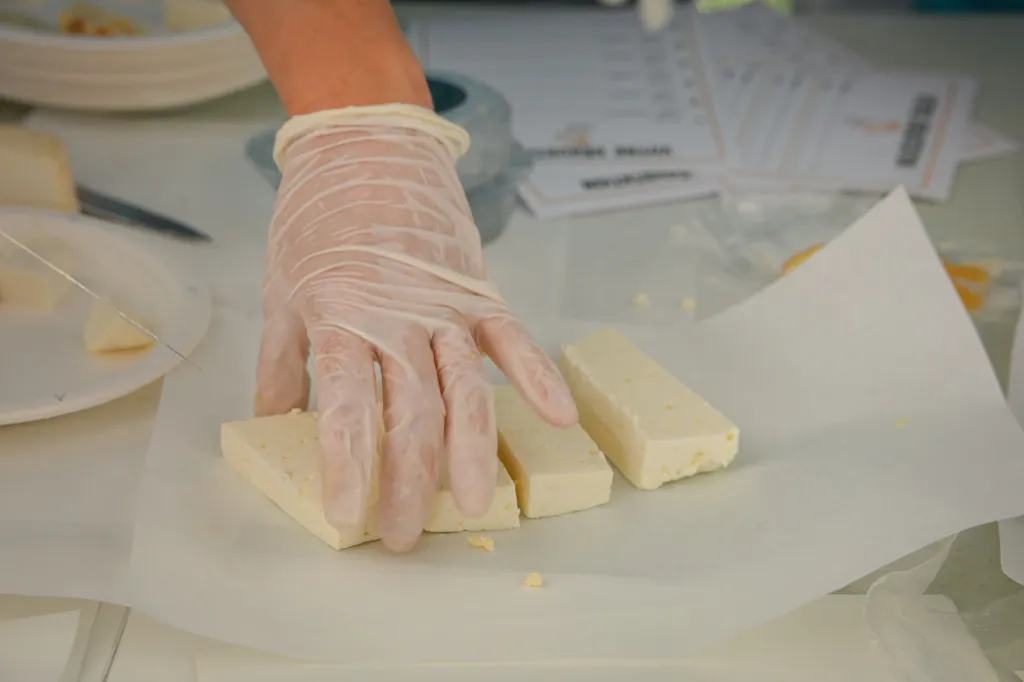 A gloved hand arranging rectangular blocks of goat cheese on a sheet of parchment paper.
