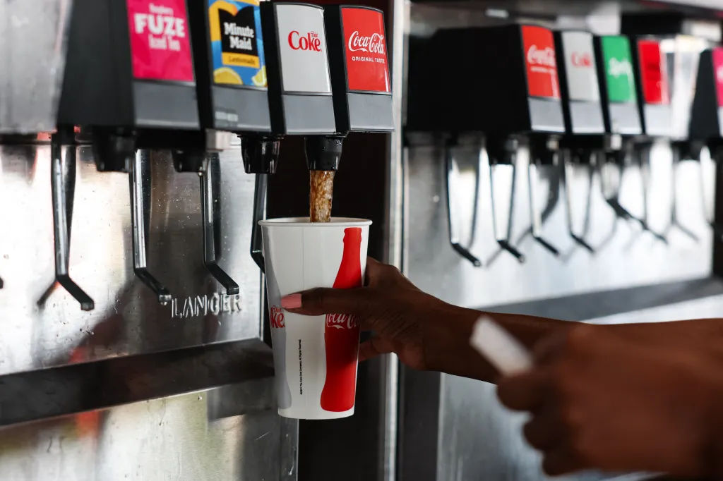A customer filling a Coca-Cola cup at a soda fountain.