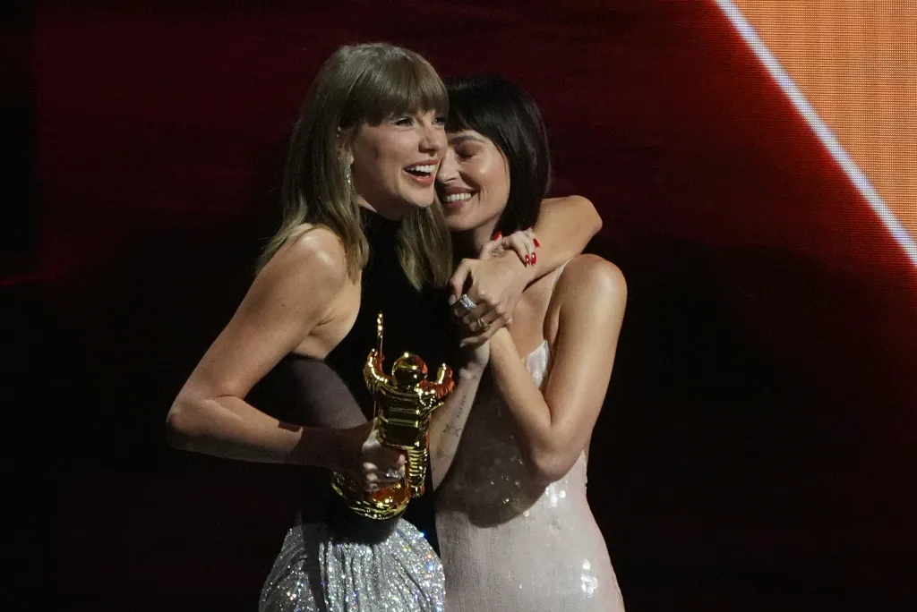 Taylor Swift, holding a golden MTV VMA award, embraces Dakota Johnson.