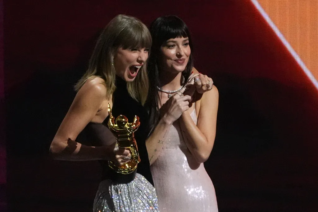 Taylor Swift holding an award, with her arm around Dakota Johnson.