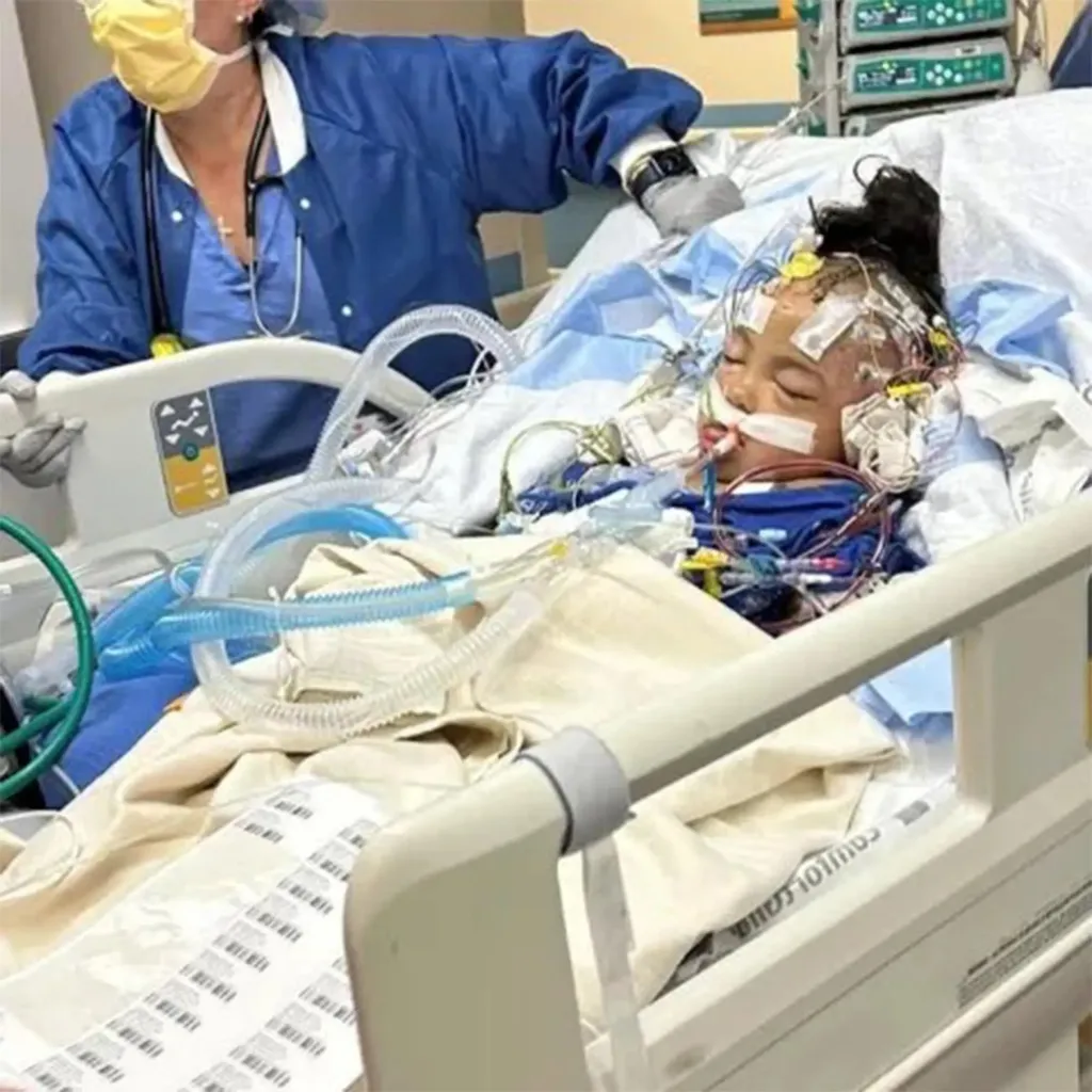 Dalilah Coleman in a hospital bed with medical tubes and wires attached to her face and head.