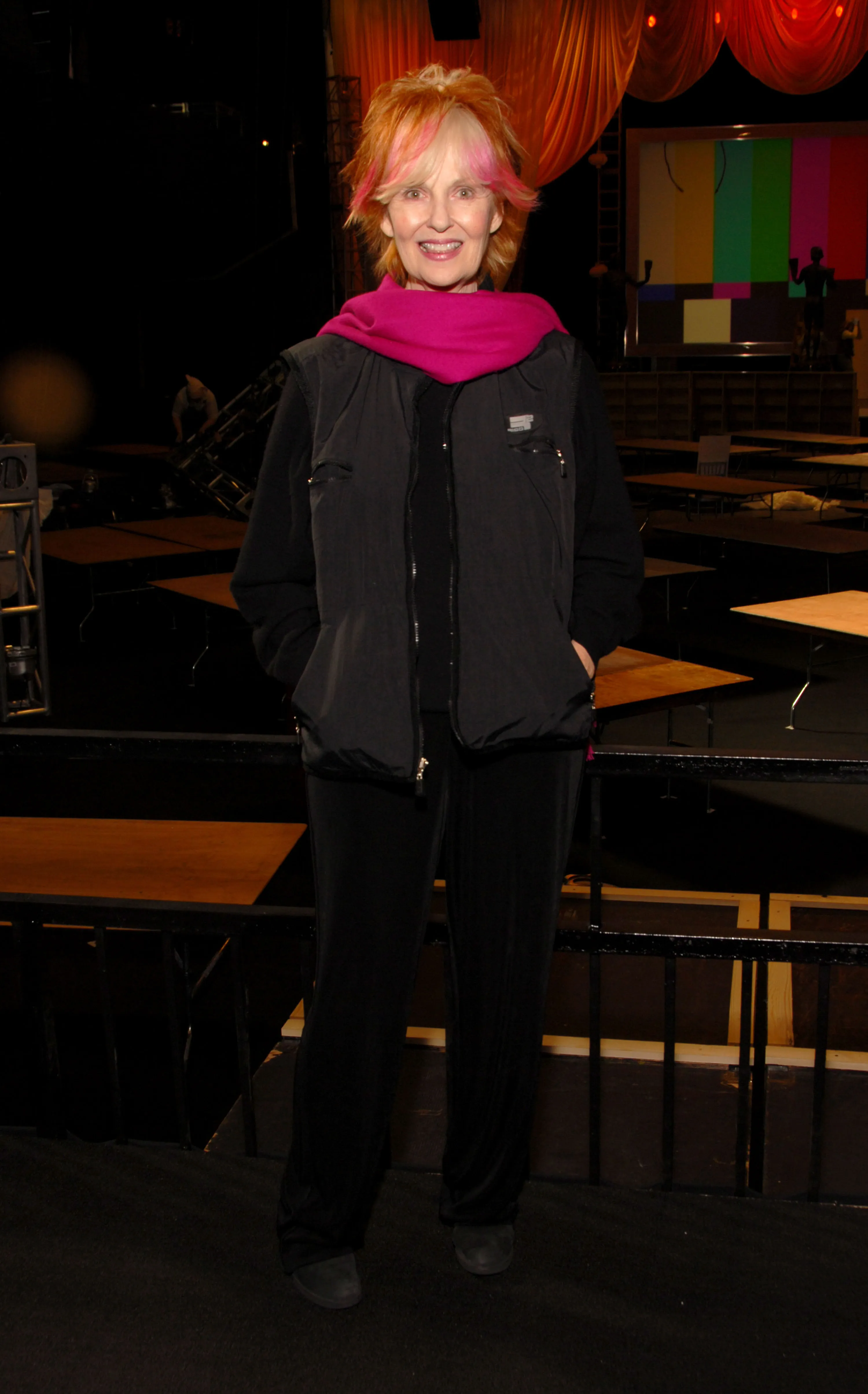 Shelley Fabares smiling in a black vest and pink scarf, backstage at an event.