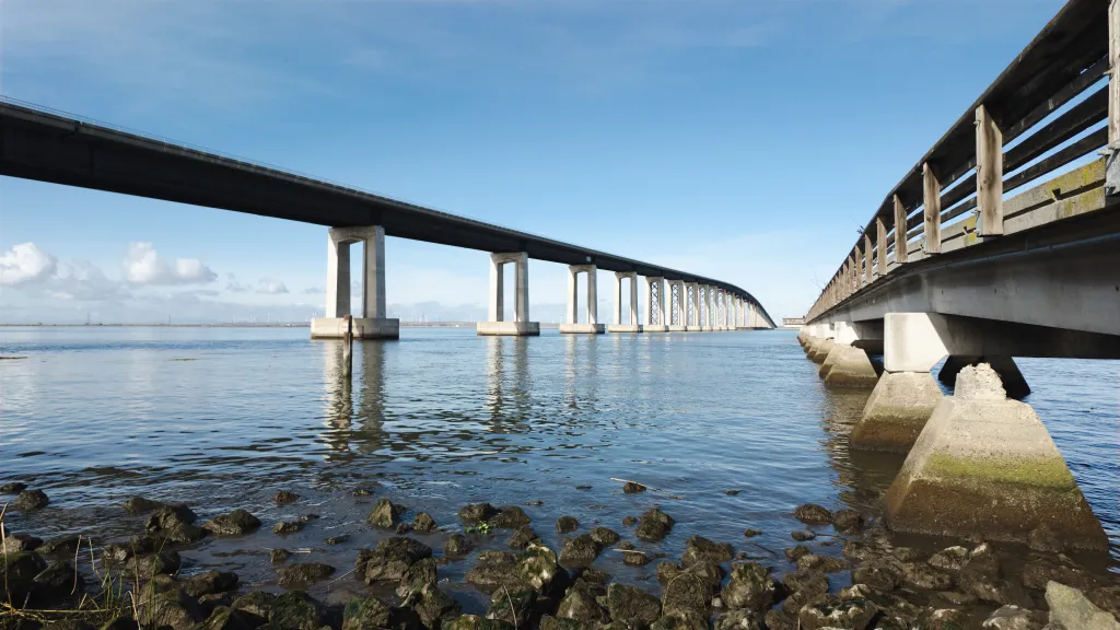The Antioch Bridge in the Delta Region of California spans over water with concrete supports, next to an older wooden pier.