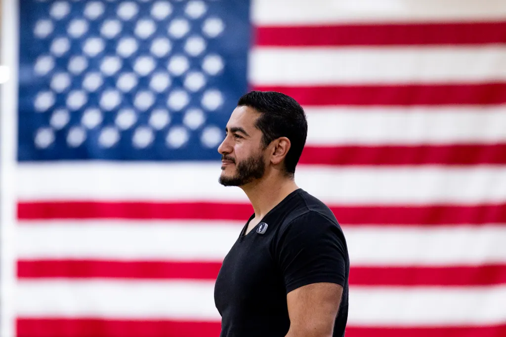 Abdul El-Sayed listening at a town hall event with an American flag in the background.
