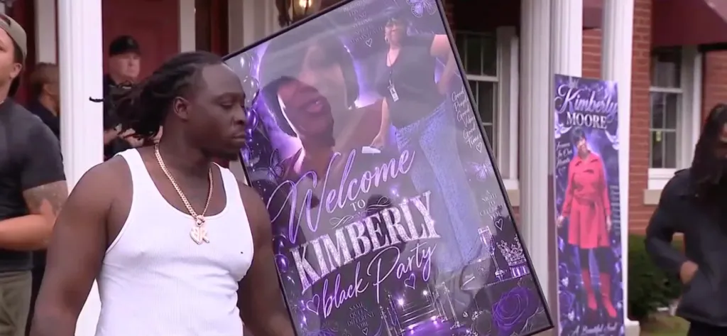 A man holding a welcome sign for Kimberly's Black Party and a banner for Kimberly Moore, who was mistakenly cremated.