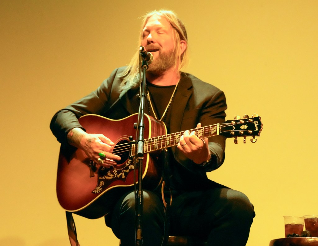 Devon Allman performs on acoustic guitar and sings into a microphone.
