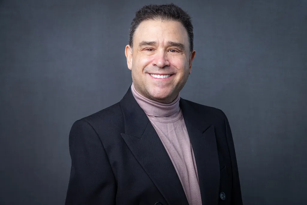 Mason Blake Pimsler, MD, smiling in a black suit jacket and a light pink turtleneck.