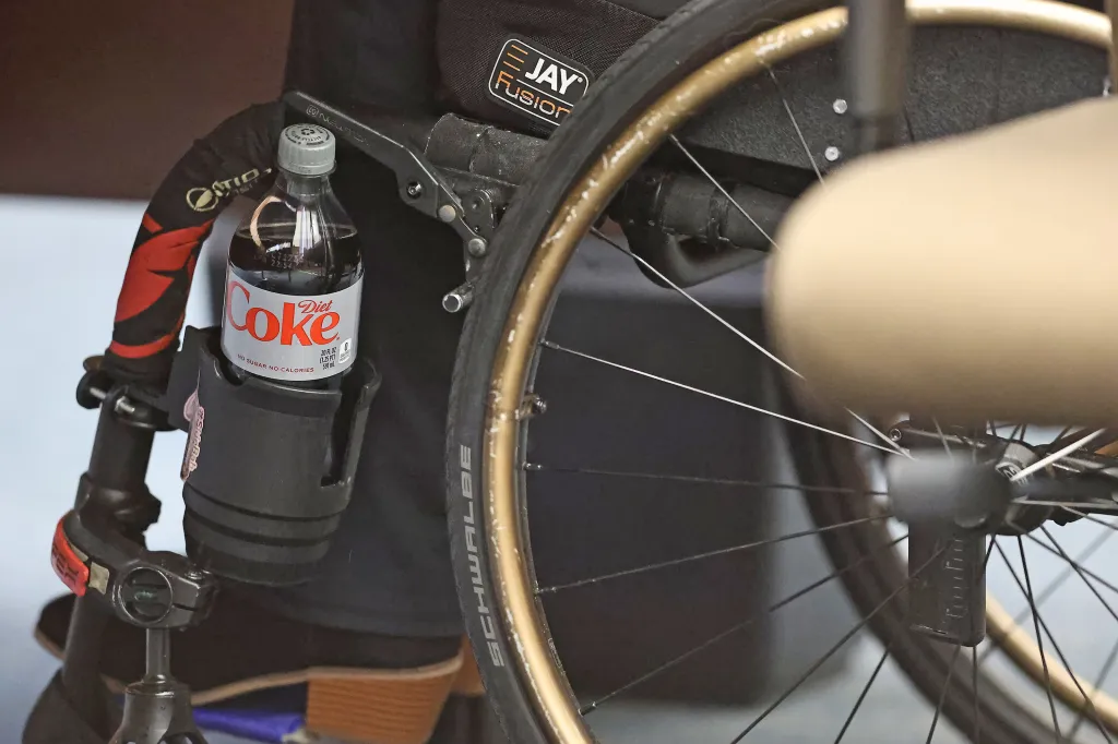 A bottle of Diet Coke in a cup holder attached to a wheelchair.